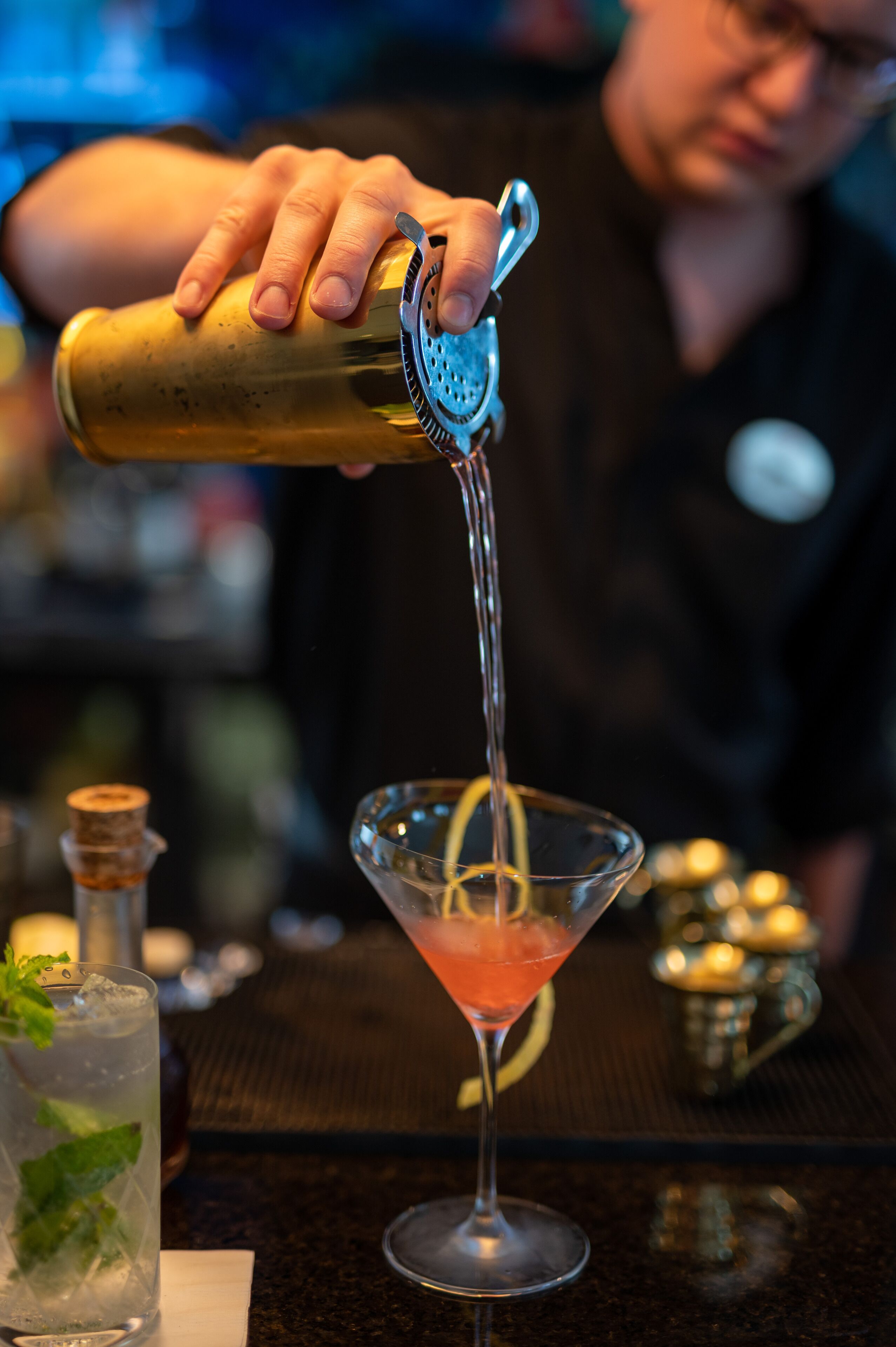 A bartender pouring a drink into a martini glass.