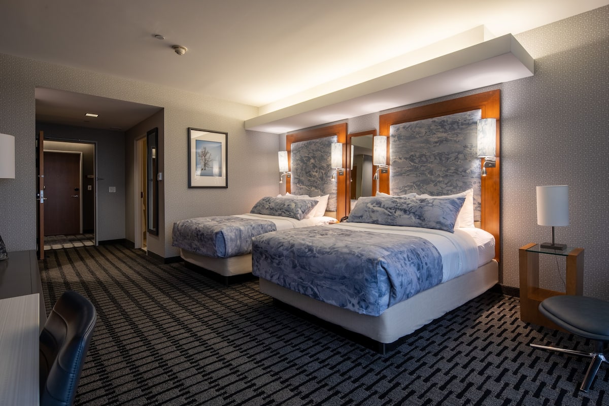 A hotel room with two beds, a desk, and a chair.