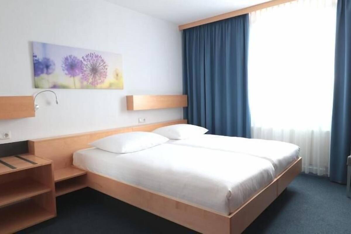 A hotel room with a bed, a chair, a desk, and a painting on the wall.