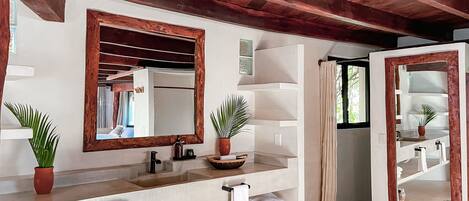 A bathroom with a wooden ceiling, a large mirror, a sink, a towel rack, and a potted plant.