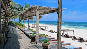 A wooden deck with lounge chairs and umbrellas overlooking a beach. - Amansala (Tulum)