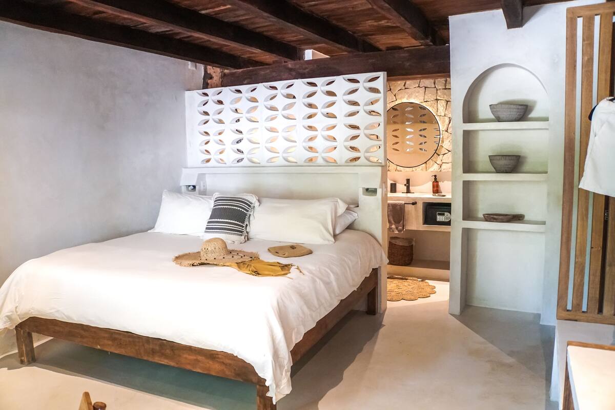 A bedroom with a wooden bed, white bedding, a decorative headboard, and a small shelf with bowls.