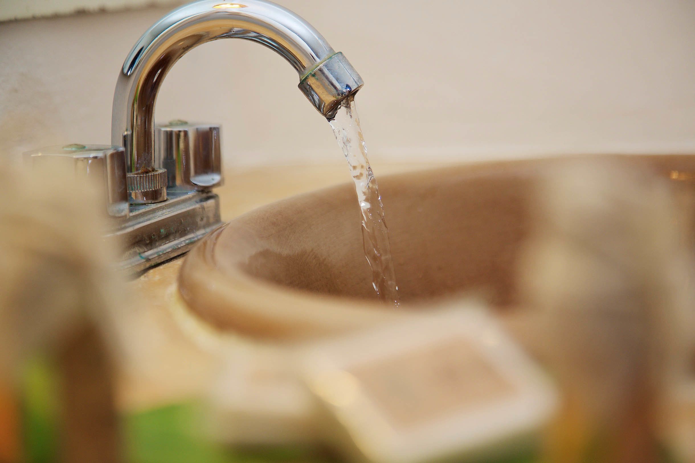 Primer plano de un grifo cromado con agua corriendo en un lavabo color beige.