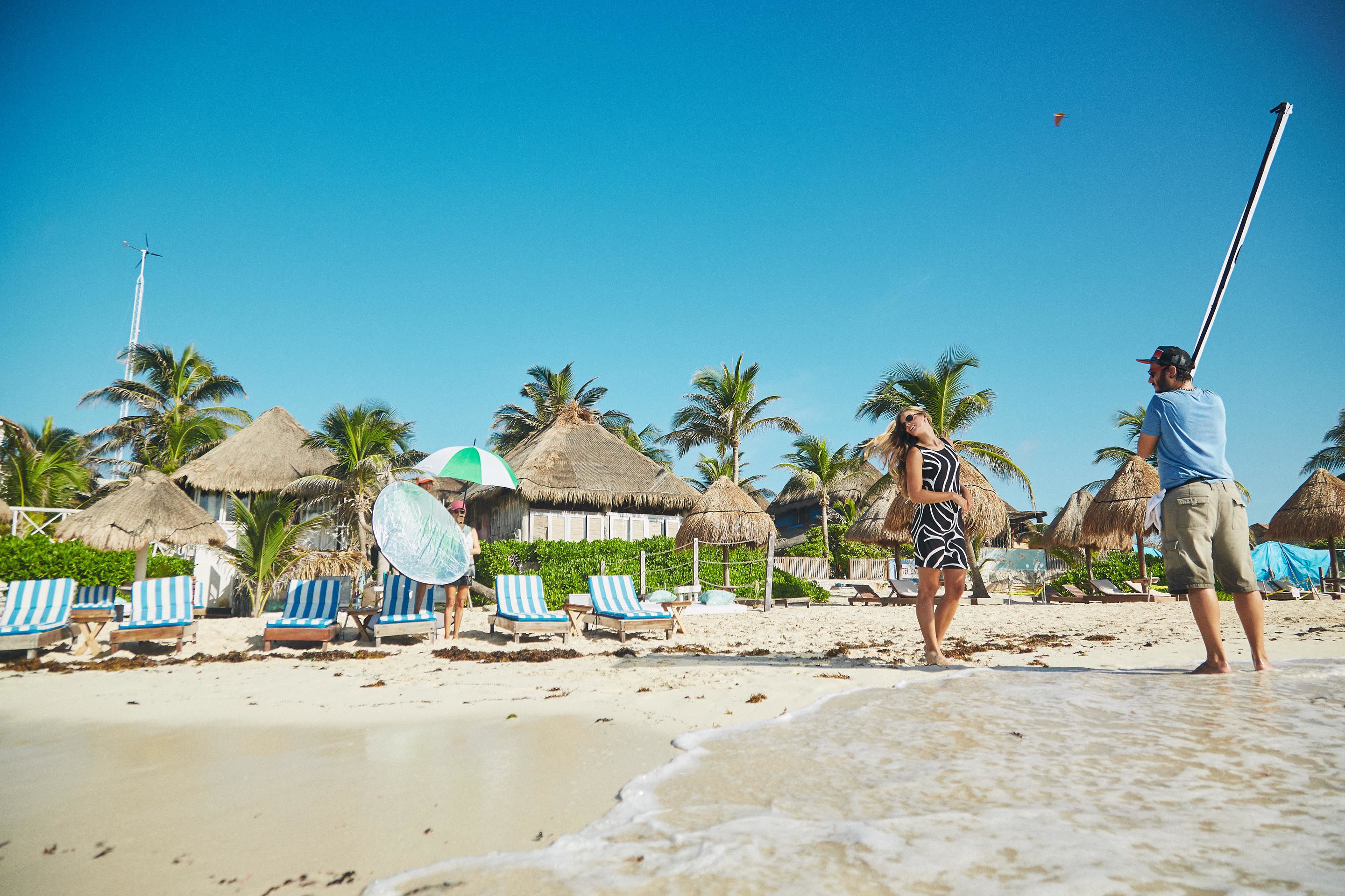 Una playa con cabañas de techo de paja, palmeras y sillas de descanso.