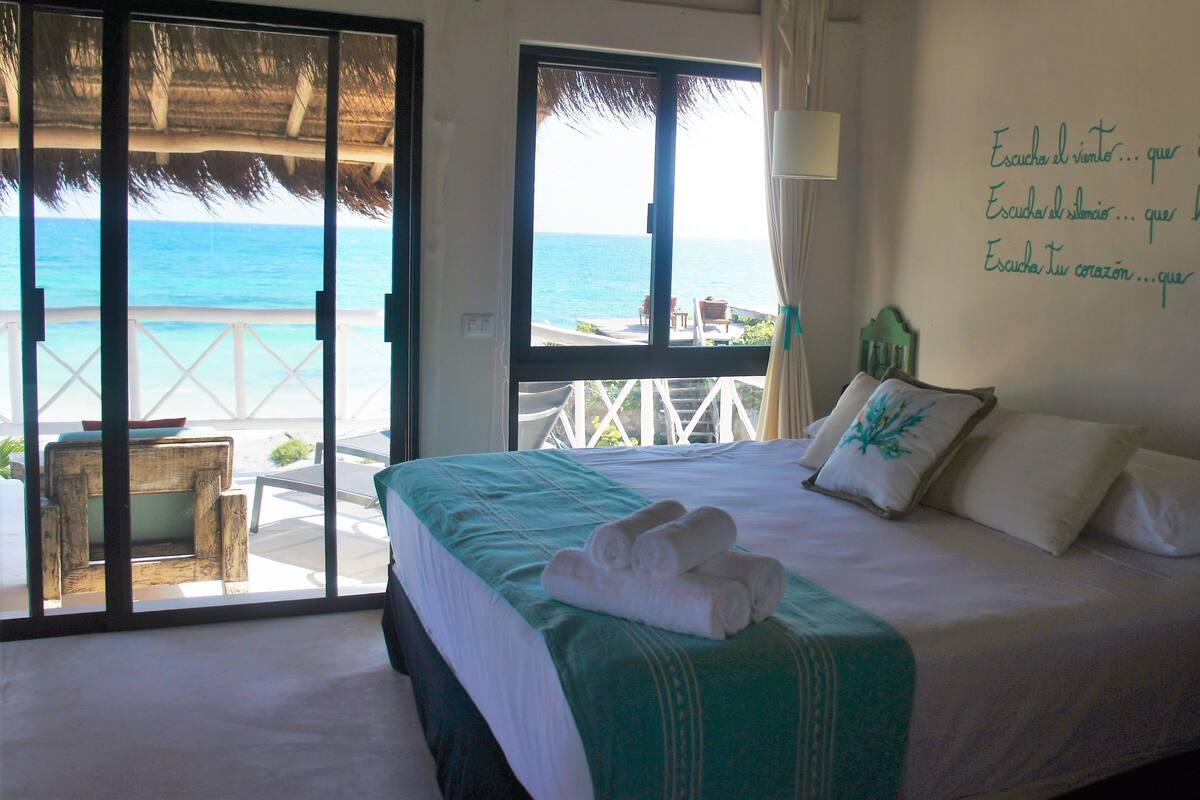 A hotel room with a bed, a view of the ocean, and a wall with inspirational text.
