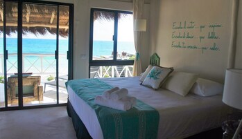 Una habitación de hotel con una cama, vistas al océano y una pared con texto inspirador.