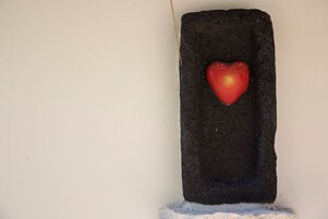 Un objet rouge en forme de cœur, incrusté dans un mur sombre à la texture marquée.