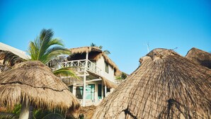 Een strandpand met rieten daken, een balkon en palmbomen.