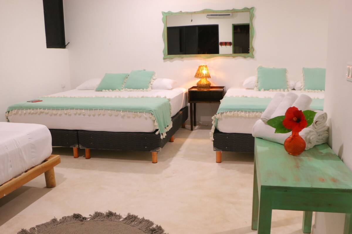 A room with two beds, a nightstand with a lamp, a small table with a vase, and a mirror on the wall.