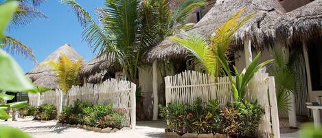 A tropical resort with thatched-roof huts, palm trees, and a sandy pathway.