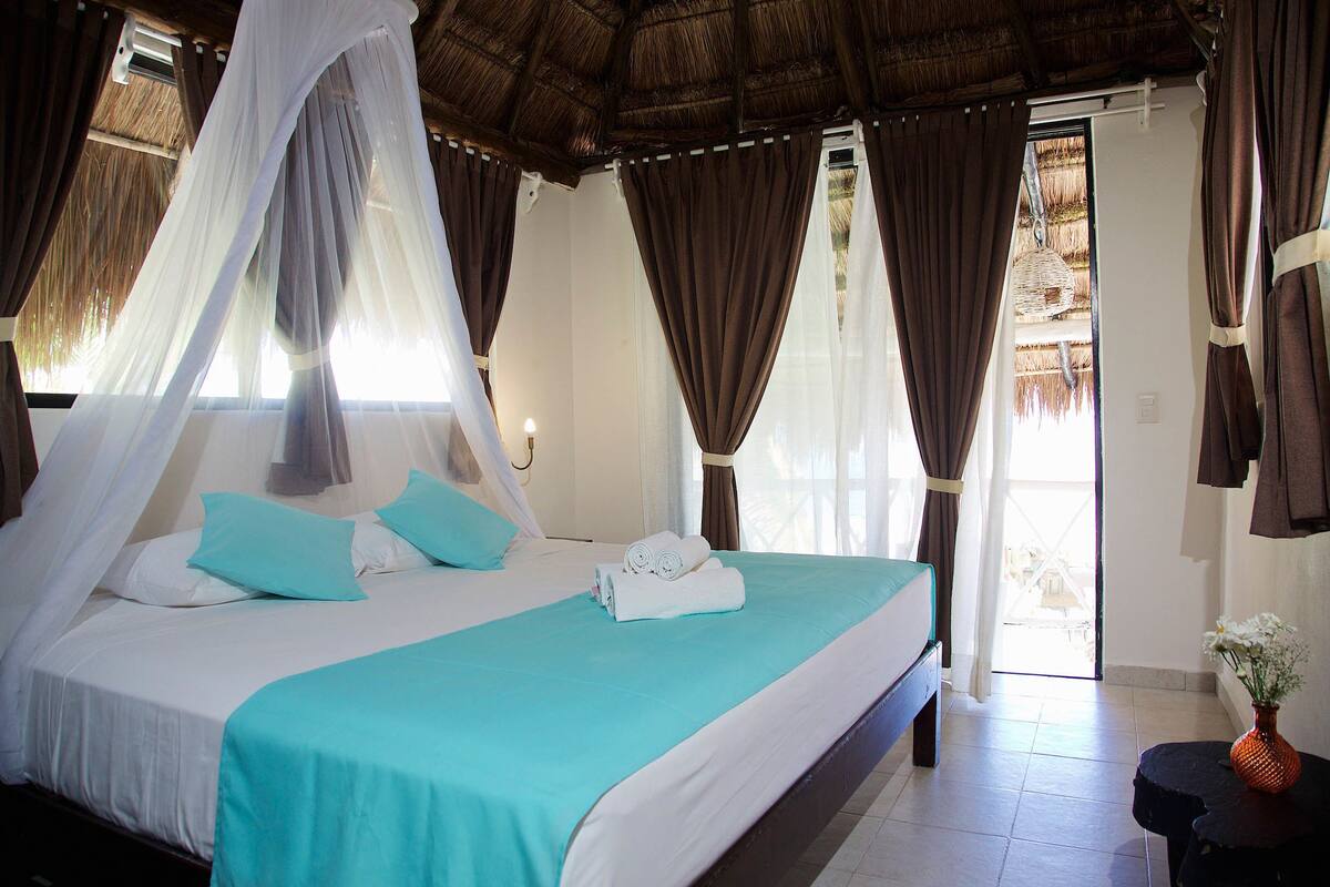 A bed with a canopy, a pair of towels, and a vase with flowers.