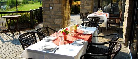 An outdoor patio with tables set for dining, stone walls, and a view of the countryside.