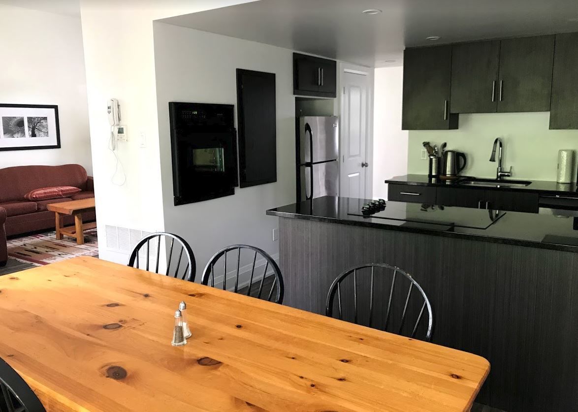 Una cocina moderna con armarios oscuros, un refrigerador de acero inoxidable y una mesa de comedor de madera con sillas.