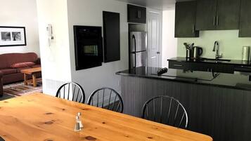Una cocina moderna con armarios oscuros, un refrigerador de acero inoxidable y una mesa de comedor de madera con sillas.