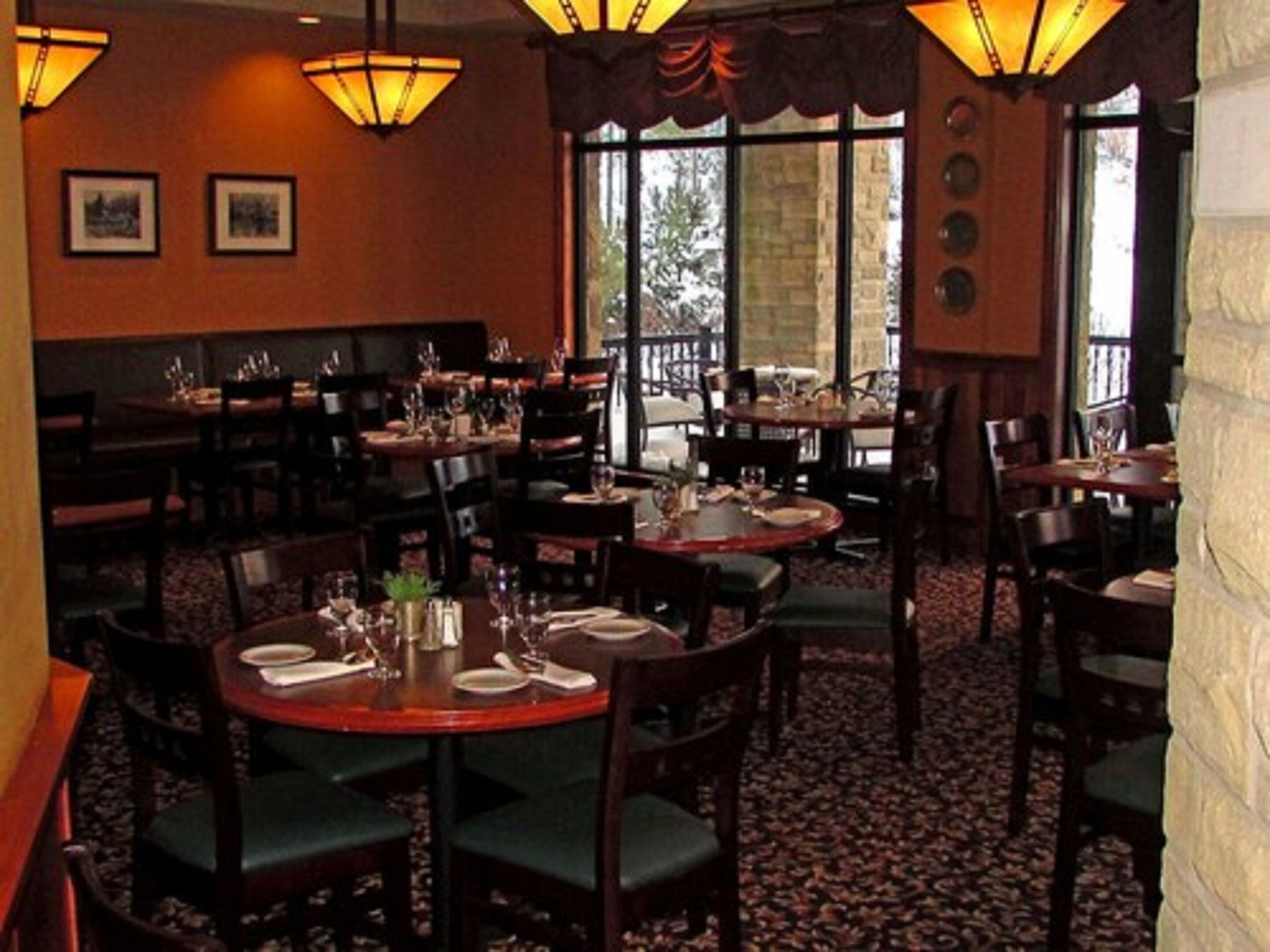 Un restaurant doté de plusieurs tables et chaises rondes, de grandes fenêtres et d’un éclairage chaleureux.