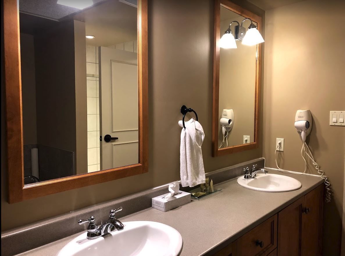 Une salle de bain avec deux lavabos, un grand miroir, un porte-serviettes et un sèche-cheveux.