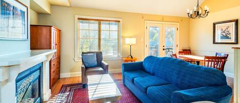 A living room with a sofa, armchair, fireplace, and a dining area with a table and chairs.
