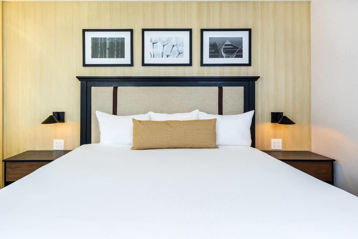 A neatly made bed with a headboard, two bedside tables with lamps, and three framed pictures on the wall.