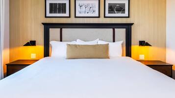 A neatly made bed with white linens and a checkered pillow, flanked by two bedside tables with lamps, against a wall with three framed pictures.