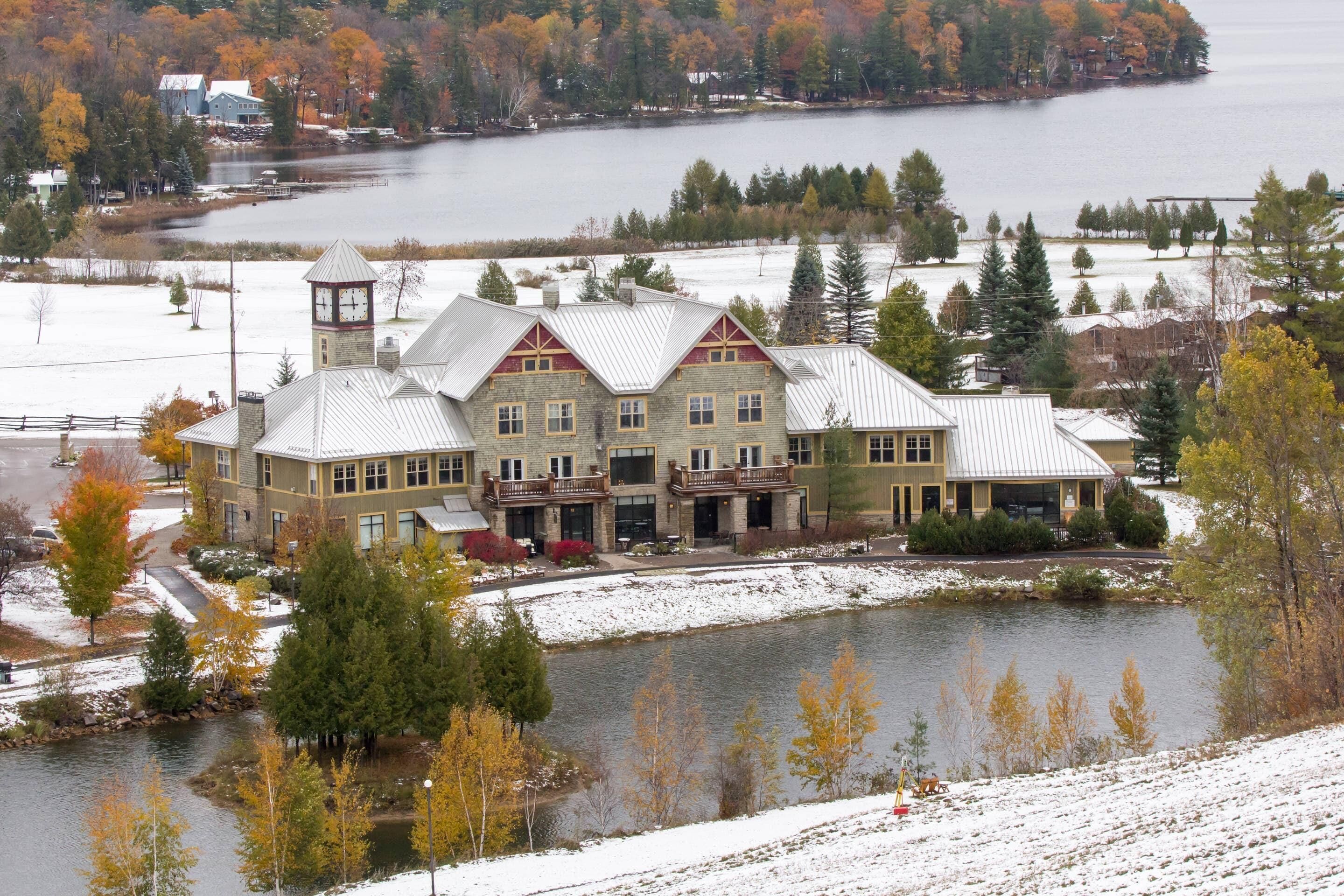 A large, multi-story building with a prominent clock tower, situated by a lake with a snow-covered landscape.