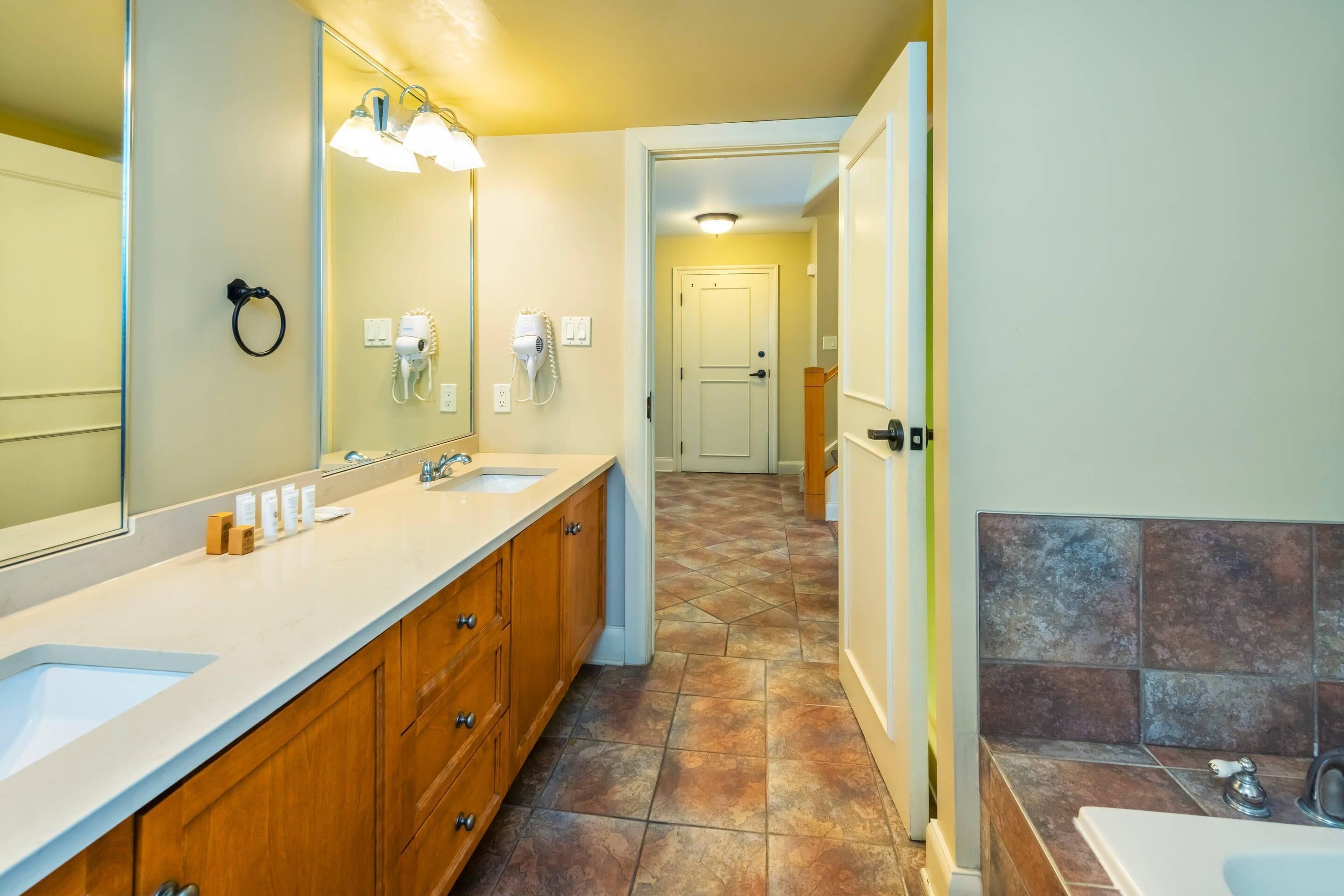 A bathroom with two sinks, a mirror, a hairdryer, and a shower area.