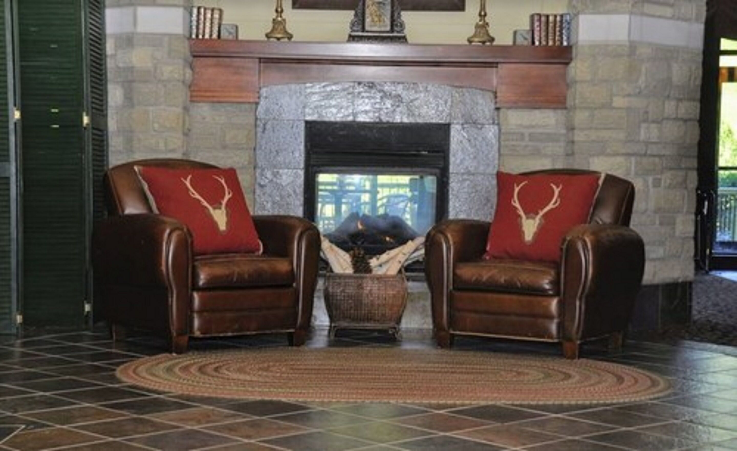 A room with two leather armchairs facing a stone fireplace, a woven rug, and a view through the window.