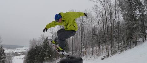Un snowboarder realizando una maniobra en una ladera nevada con árboles al fondo.