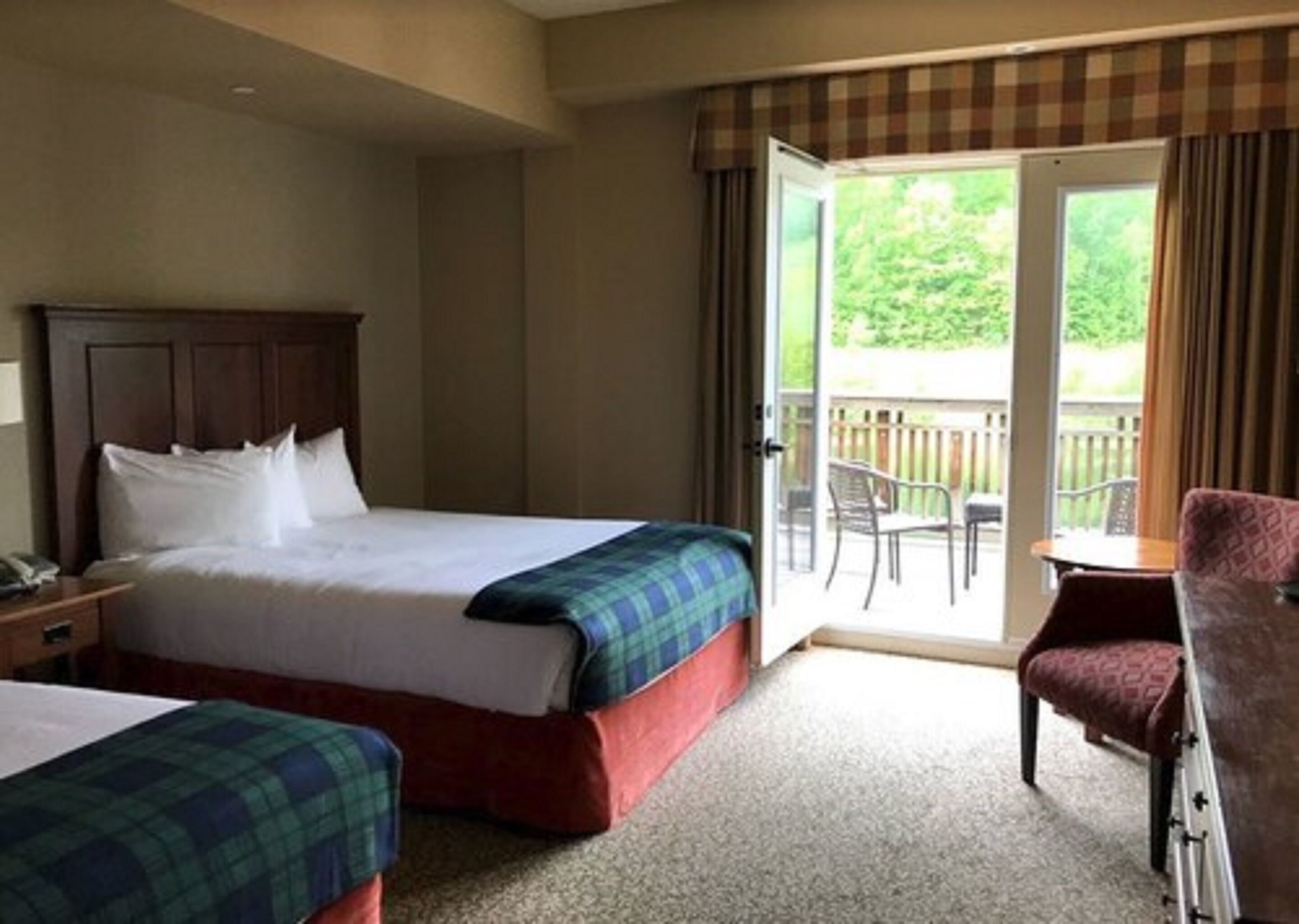 A hotel room with a bed, a chair, and a balcony with a view of greenery.