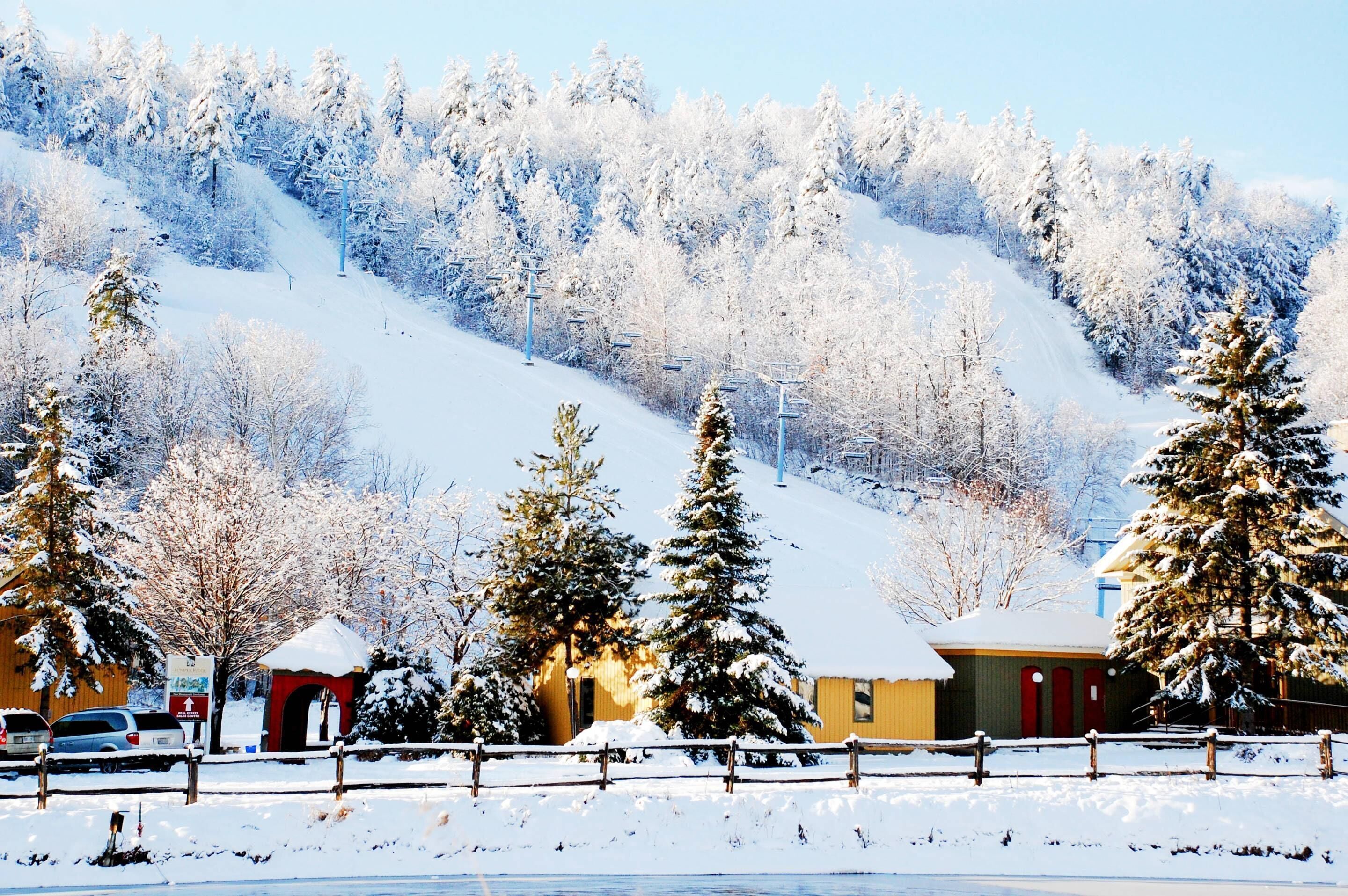 A snow-covered landscape with a ski lift, a wooden cabin, and a red building.