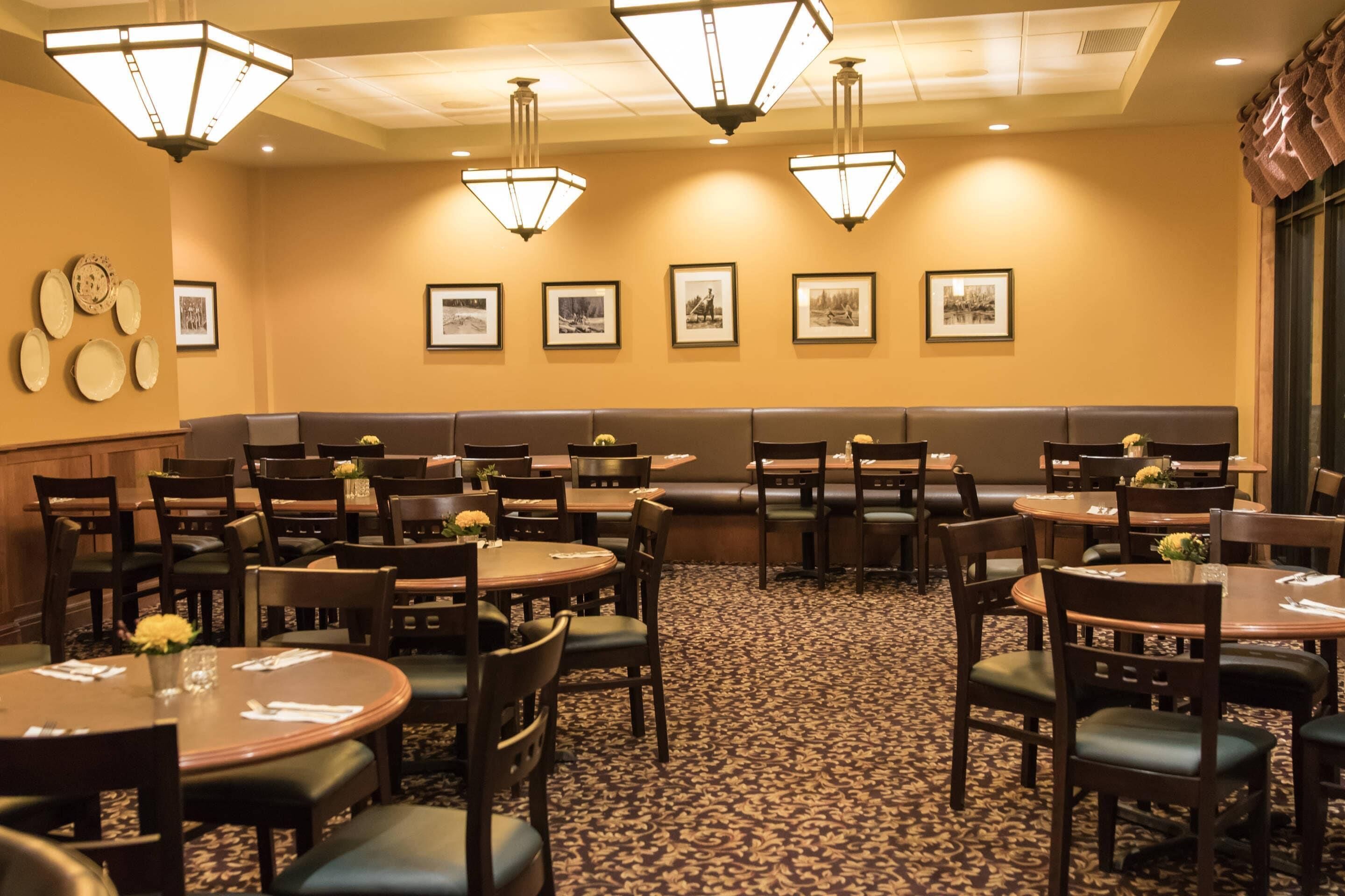 A restaurant with multiple tables and booths, framed pictures on the wall, and a patterned carpet.