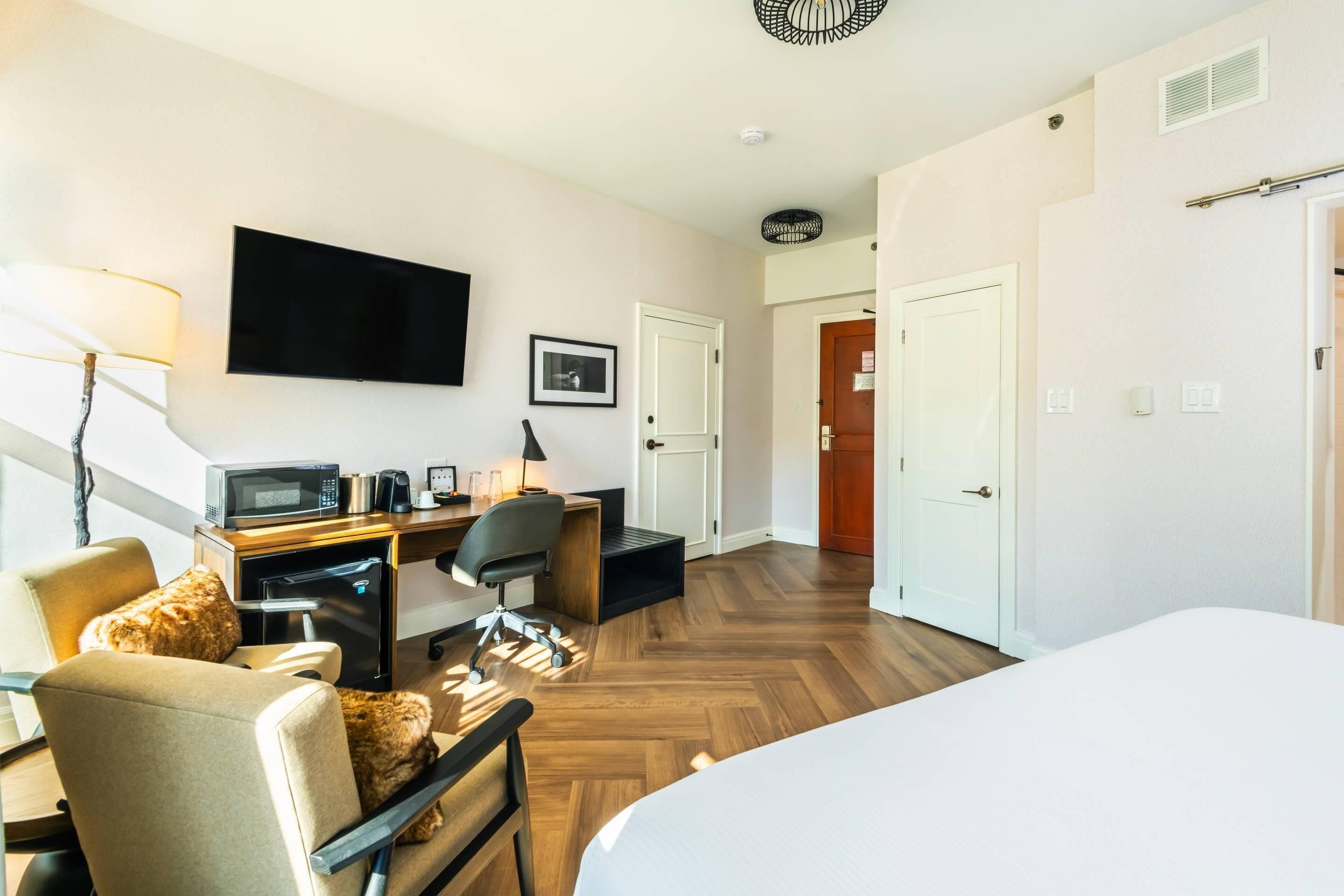 A hotel room with a bed, desk, chair, television, and a door.