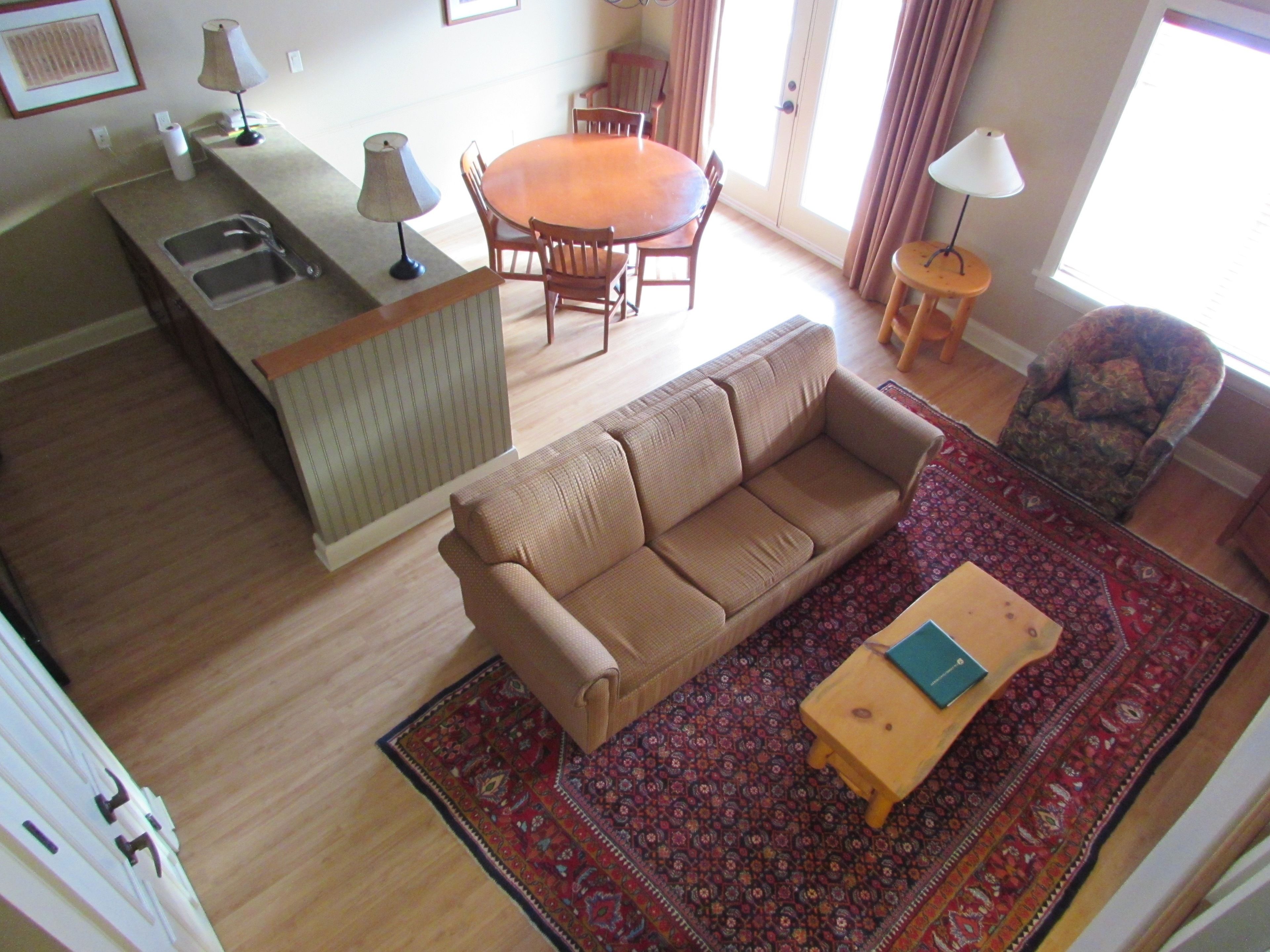 A living room with a sofa, a small wooden table, a patterned rug, and a dining area with a table and chairs.
