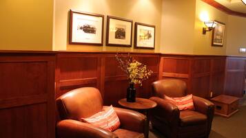 A lobby with two leather armchairs, a small table with a vase, and framed pictures on the wall.