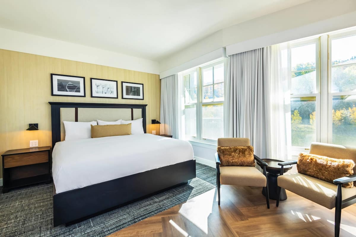 A hotel room with a large bed, a sofa, a small table, and a window with curtains.