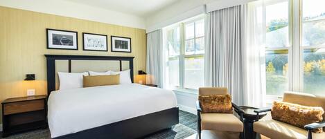 Una habitación de hotel con una cama grande, un sofá, una mesita y una ventana con cortinas.