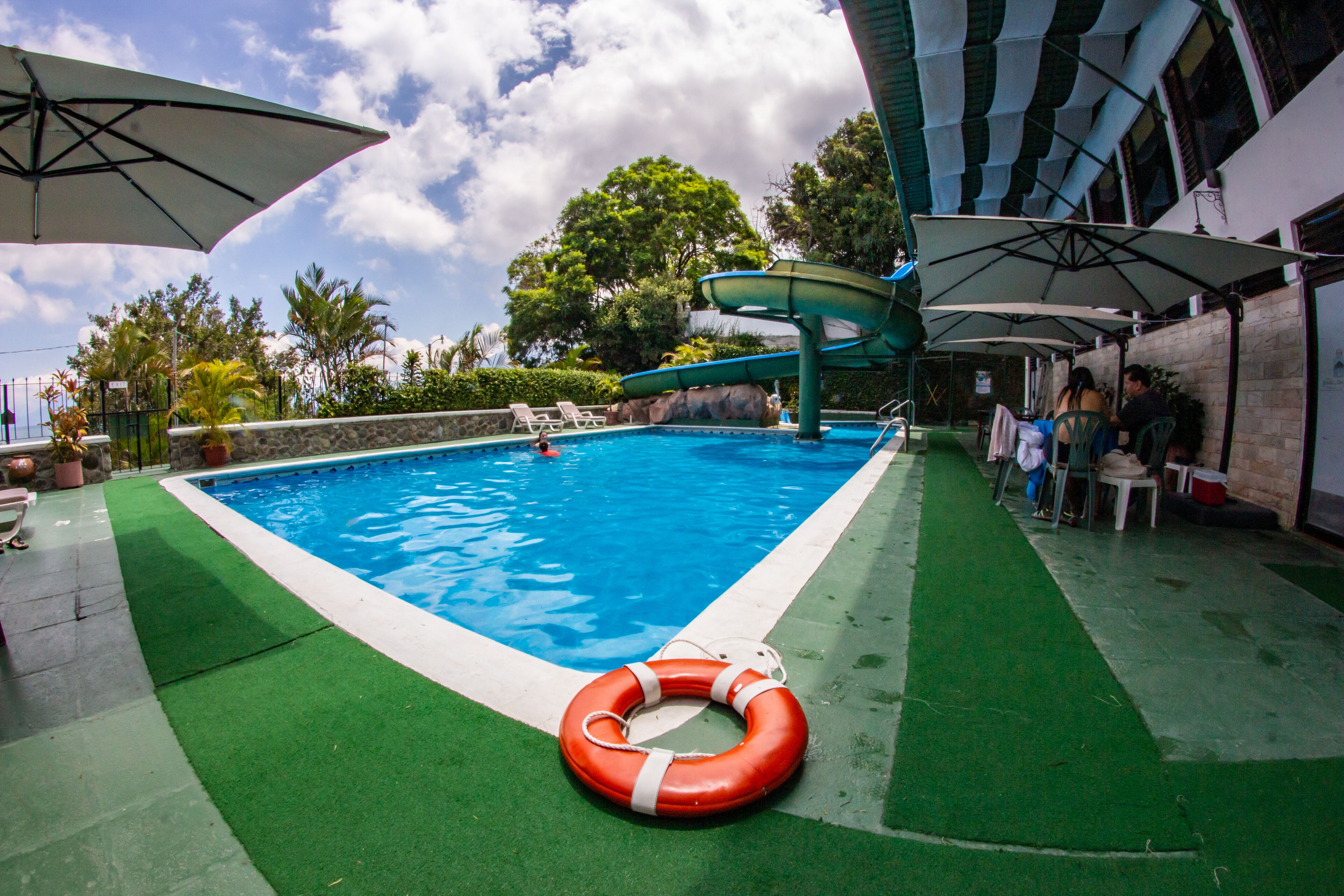 A swimming pool with a water slide, surrounded by umbrellas and lounge chairs.
