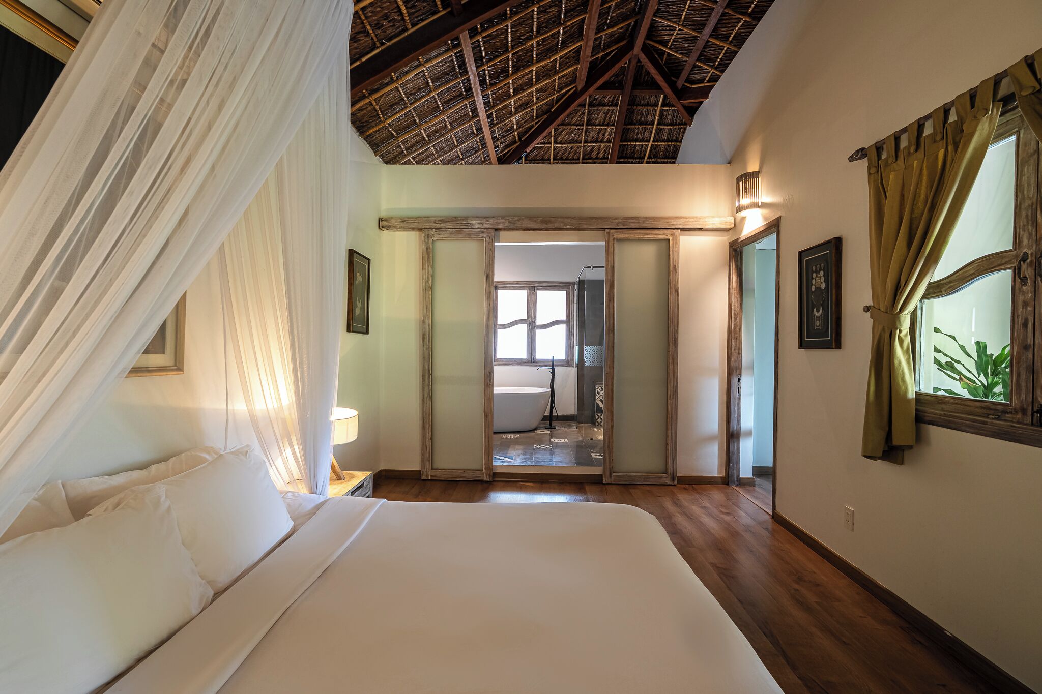 A bedroom with a large bed, a canopy, a wooden ceiling, and a view of a bathroom.