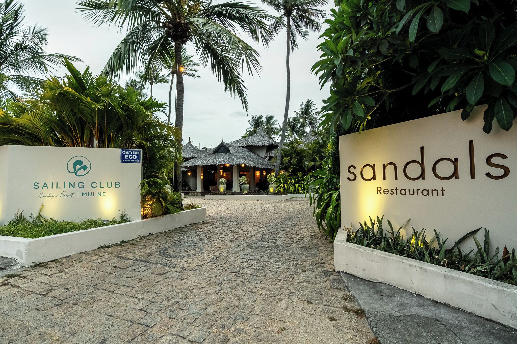 Ein Weg, der zu einem Gebäude führt, mit einem Schild für 'Sailing Club Boutique Resort' und 'Sandals Restaurant'.