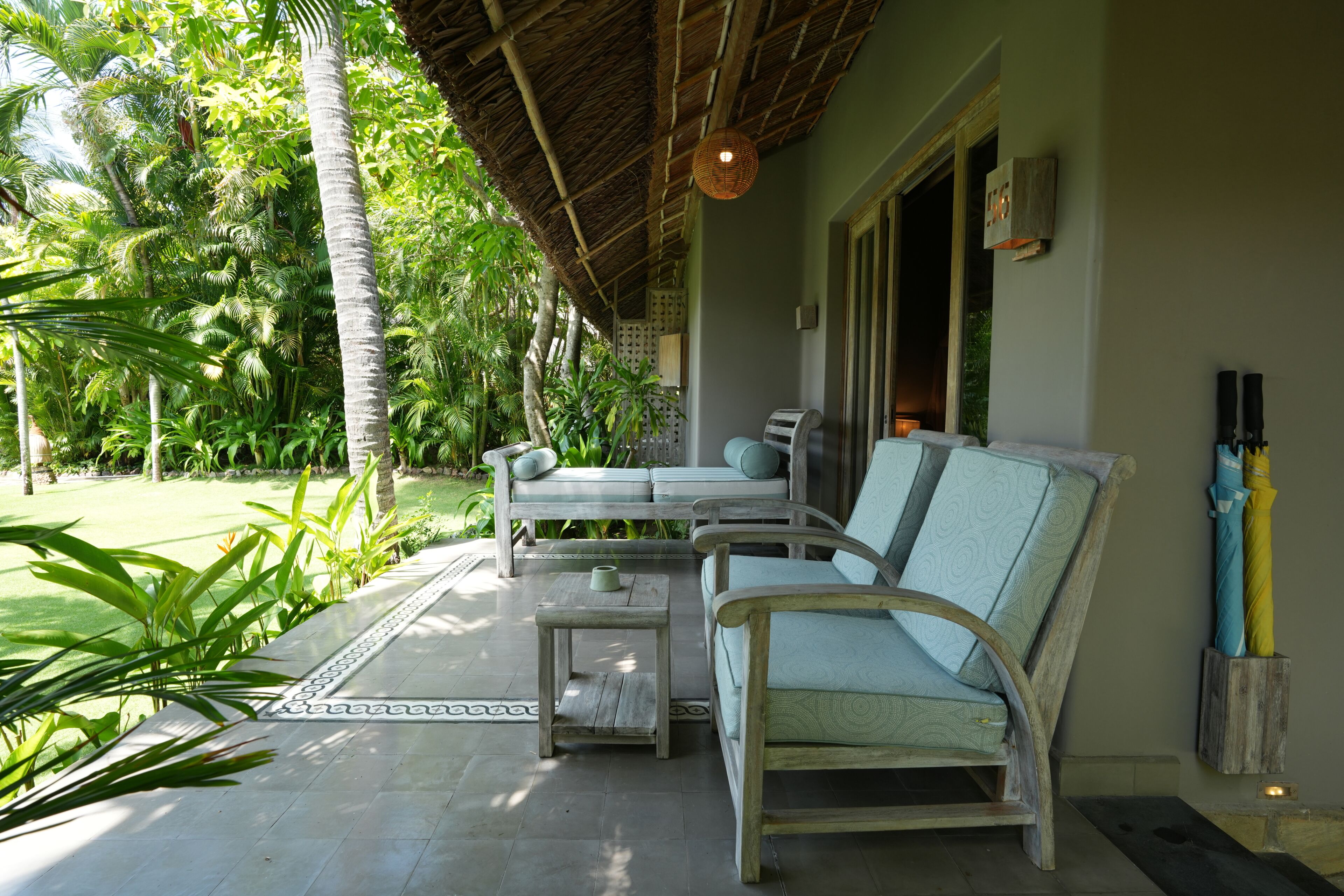 A covered outdoor seating area with a sofa and chairs, a small table, and a decorative wall-mounted light fixture.