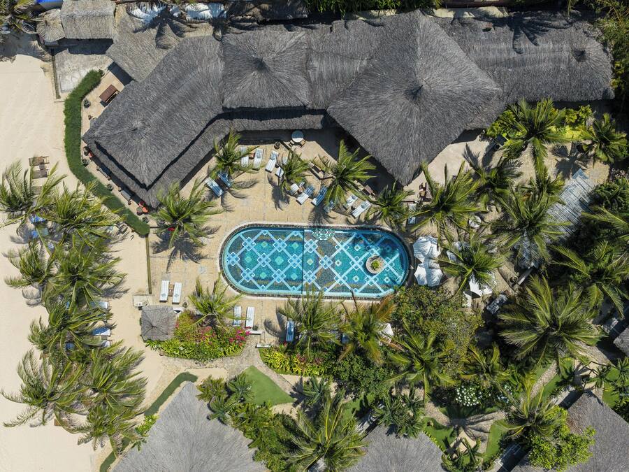 An aerial view of a resort with a swimming pool surrounded by palm trees and lounge chairs.