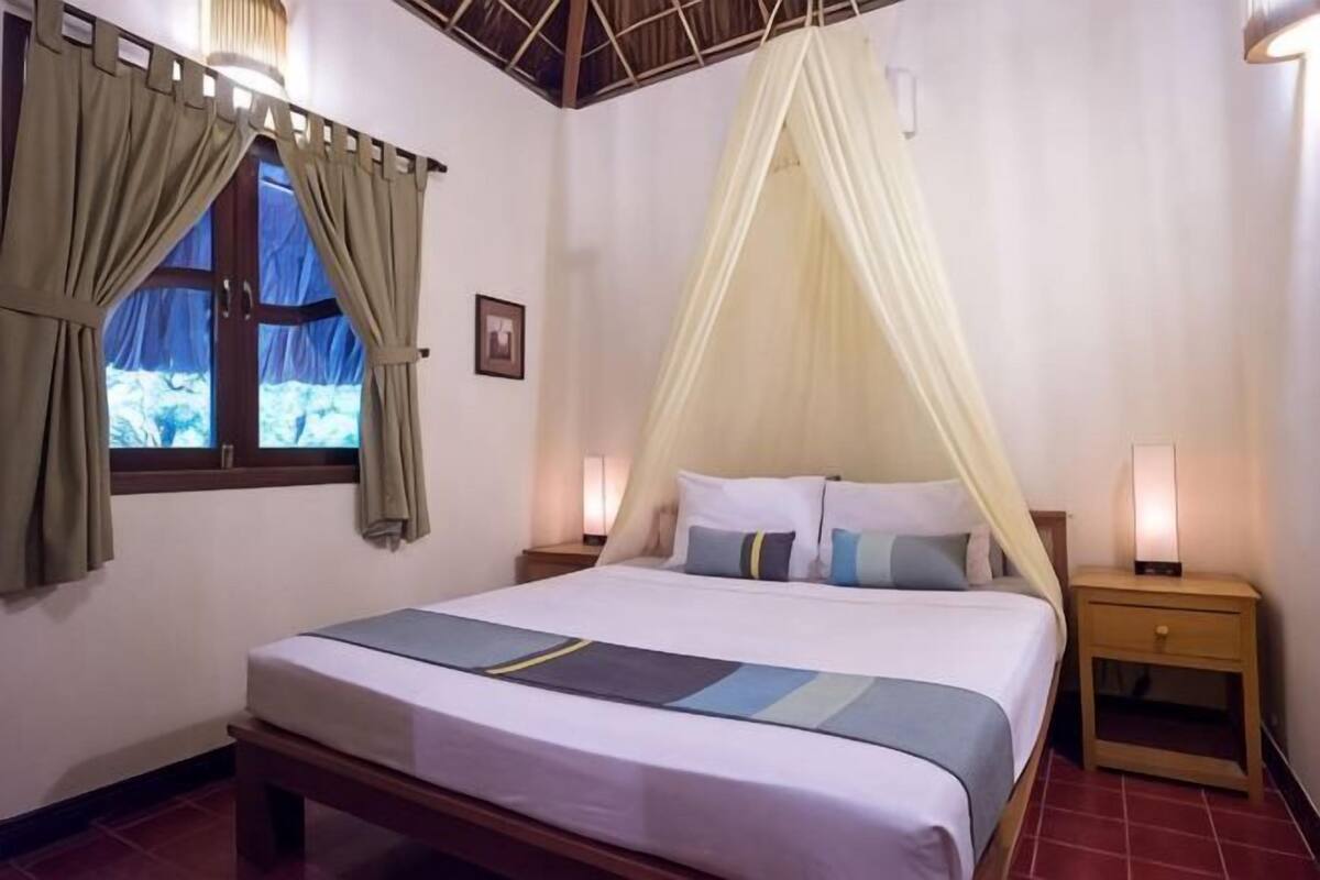 Quarto com cama, cortinas, dossel, abajures e janela com vista.