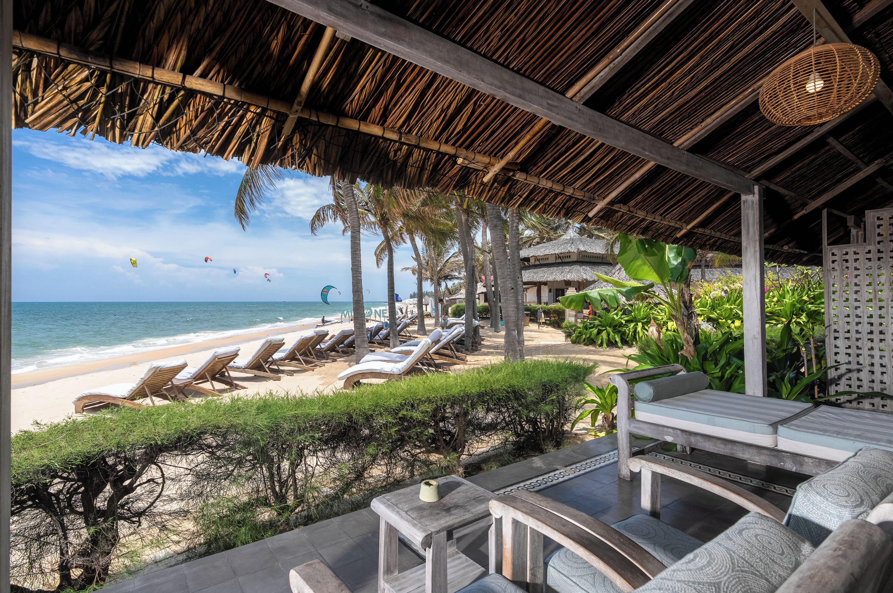 A beachside lounge with sun loungers, a thatched roof, and a view of the ocean.