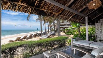 A beachside lounge with sun loungers, a thatched roof, and a view of the ocean.