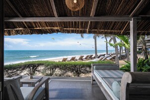 Un espacio de descanso junto a la playa, con vista al océano, sillas de descanso y una estructura de techo de paja.