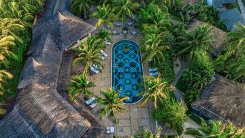 Vista aérea de un resort con piscina central, rodeado de palmeras y estructuras de techo de paja.