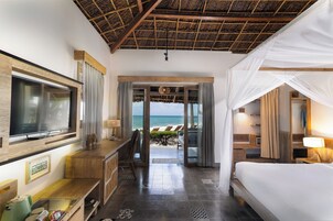 A hotel room with a bed, a desk, a TV, and a view of the beach.
