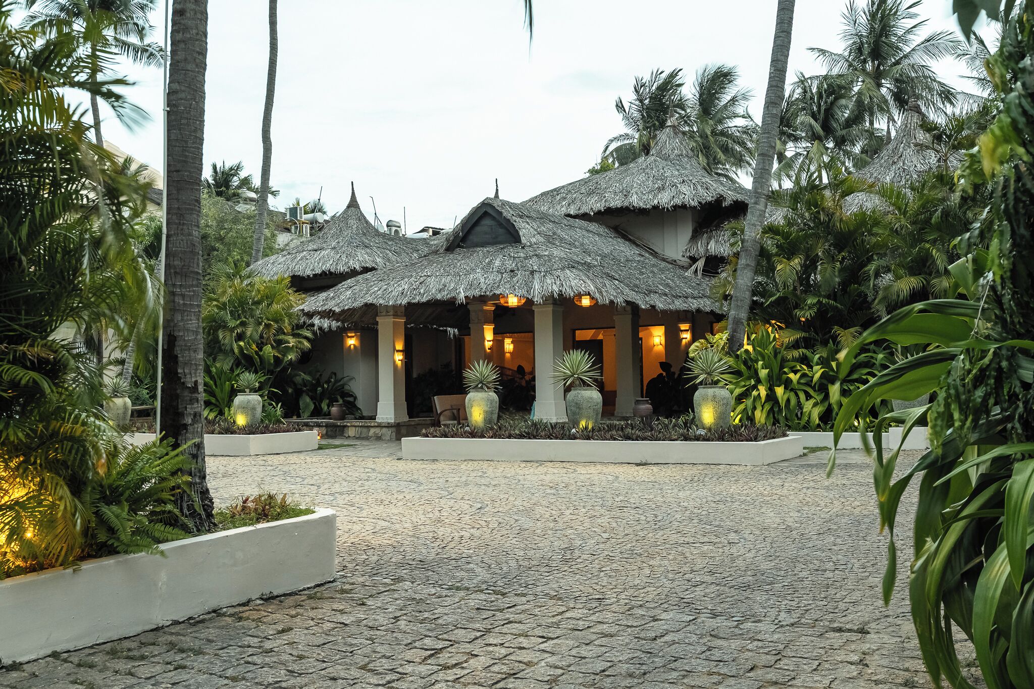 A resort with thatched-roof structures, a cobblestone pathway, and tropical vegetation.