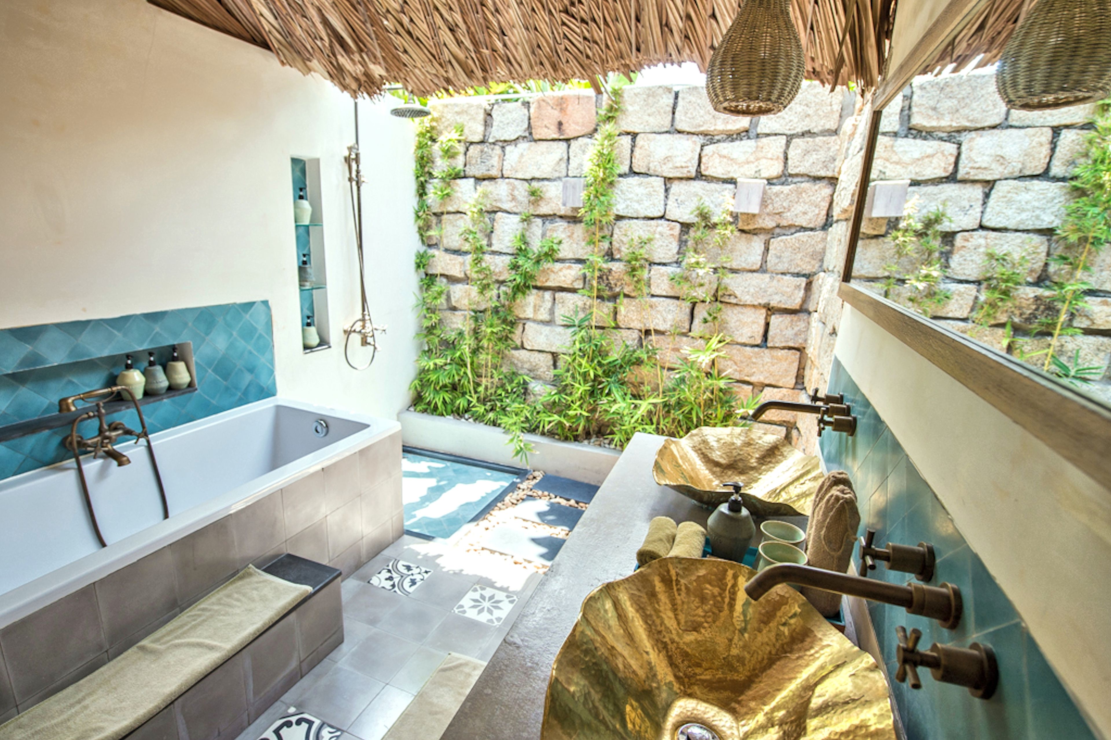 A bathroom with a bathtub, a shower, and a sink. There is a stone wall with plants growing on it.