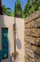 Una ducha con pared de piedra y repisa con artículos de aseo.