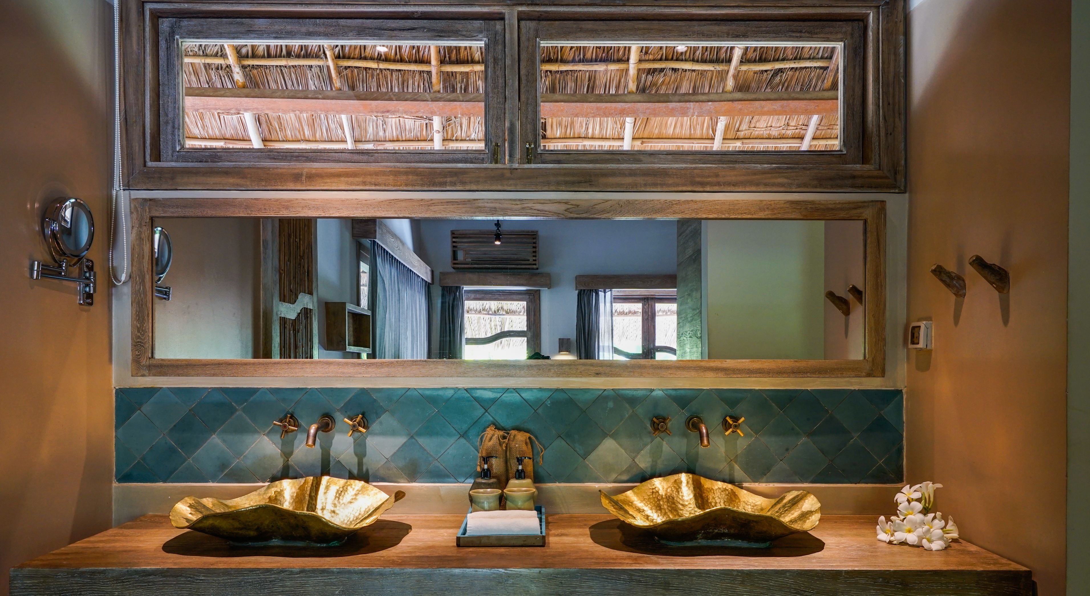 A bathroom with a large mirror, two sinks with gold basin handles, a towel rack, and a decorative wall panel.